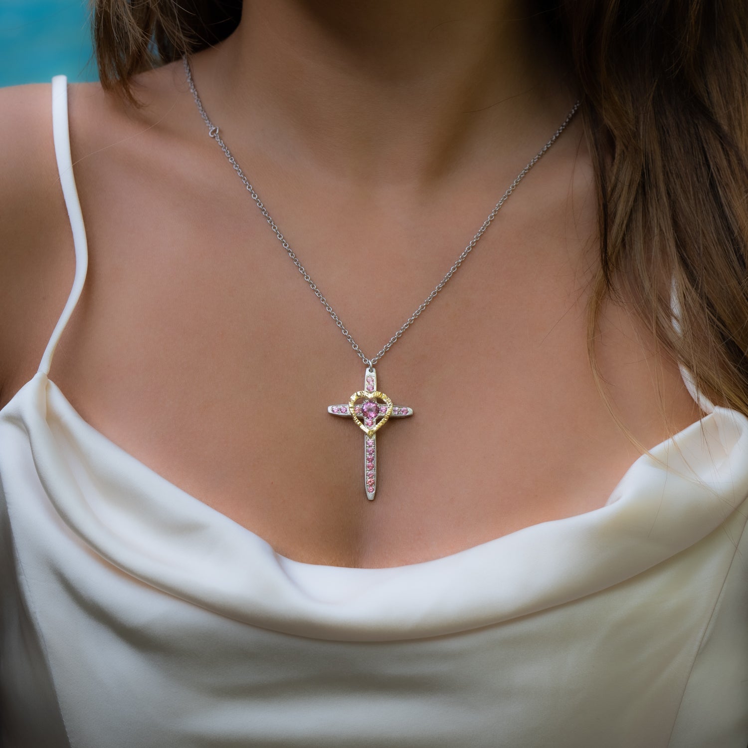 Taru Jewelry Cross and Heart Necklace crafted from 18K gold and silver is a unique blend of traditional and modern design. The cross, a timeless symbol of faith and devotion, is adorned with beautiful pink topaz, adding a touch of color and elegance to the piece.